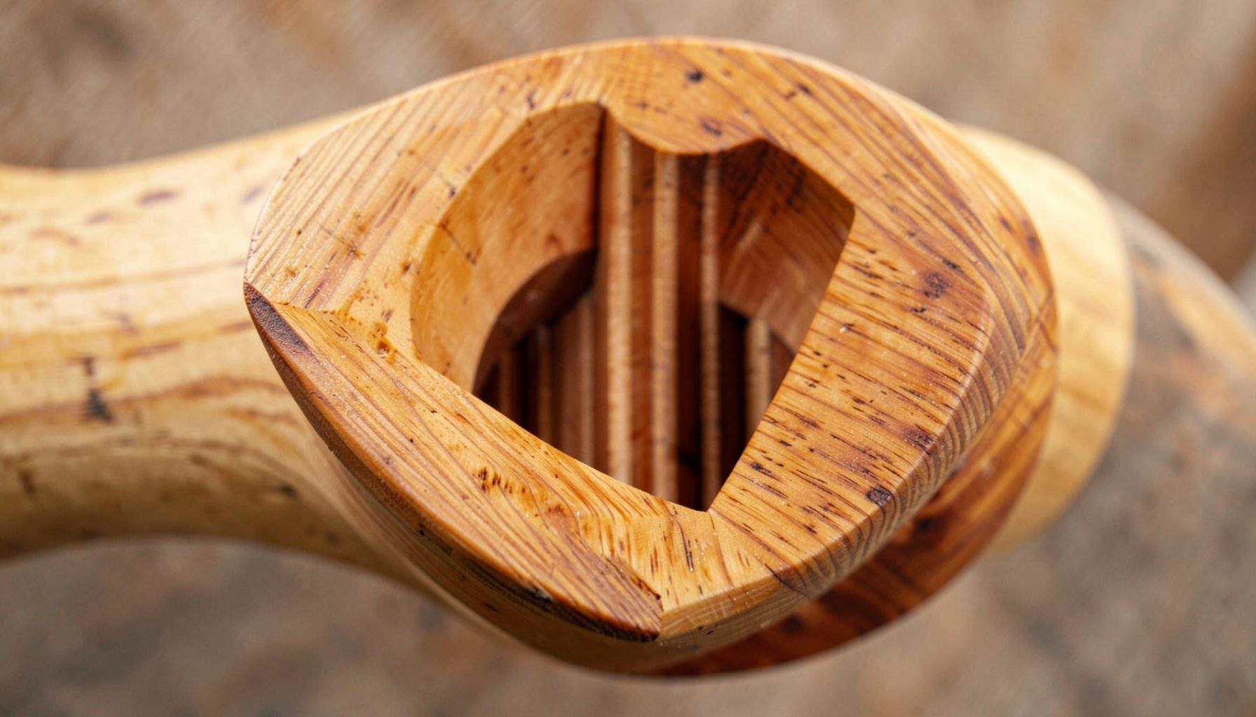 Close-up of a massive solid-wood bi-radial horn with visible layered plywood construction, warm honey-brown tones, and a multi-cellular throat with vertical fins.